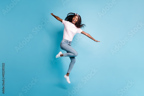 Full length photo of charming cute afro woman wear pink t-shirt jumping hands arms sides isolated blue color background