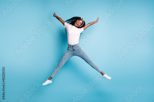 Full length photo of funny afro woman student wear pink t-shirt jumping hands arms up isolated blue color background