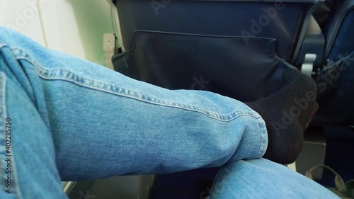 FPV of male passenger sitting on cabin chair in plane during flight. Close up of legs of relaxed passenger.