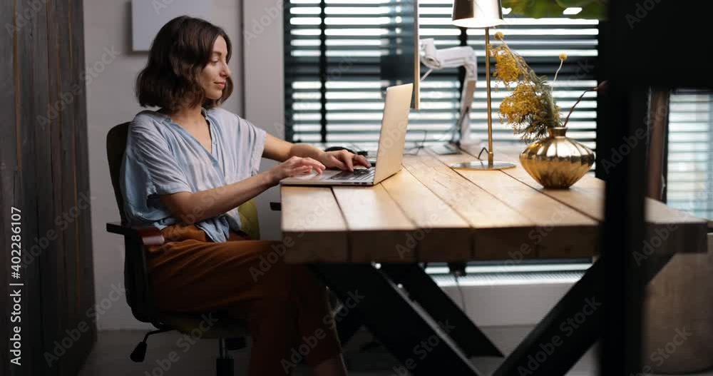 Young woman working on laptop in a cozy and style home office. Handheld shot. Stay home and happy working online from home concept