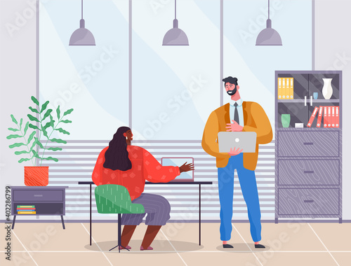 Coworkers work together. Mutually beneficial cooperation. Man in strict suit stands and holds laptop, dark-skinned woman at table with laptop. Office room, bookcase, potted plant, ceiling lighting