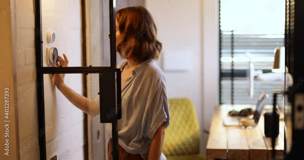 Young woman controlling room temperature with a smart thermostat at home. Medium shot. Smart home and smart heating system concept