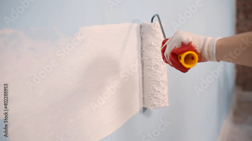 Close up of worker hand in gloves painting wall with roller