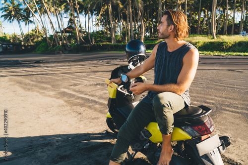 Long haired man sitting on motorbike among beach