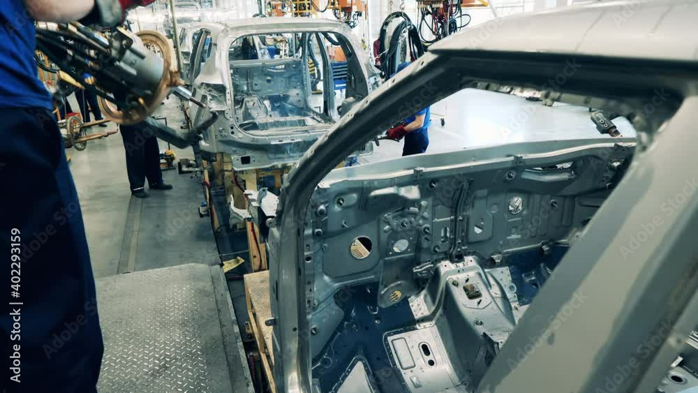 Car factory workers welding a vehicle body at a car manufacturing facility Car factory workers welding a vehicle body at a car manufacturing facility