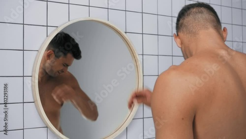 displeased man smelling armpits and grimacing in bathroom