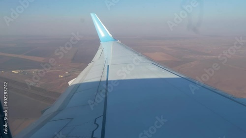View of wing upper surface and vertical stabiliser of landing aircraft. Gournd surface at background. View through plane window. photo