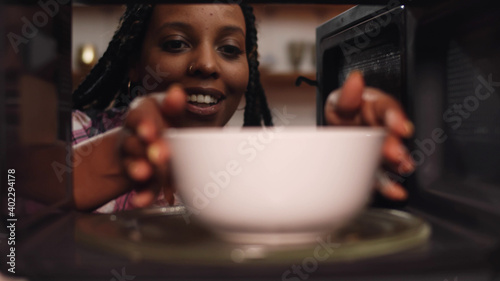 African woman reheat food in ceramic bowl using microwave oven photo