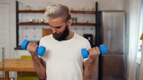 Hipster weak guy doing fitness training with dumbbells at home