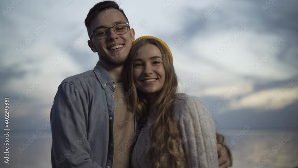 Loving young couple looking at each other, turning to camera and smiling. Portrait of relaxed Caucasian boyfriend and girlfriend dating outdoors in twilight. Bonding and romance concept. Loving young couple looking at each other, turning to camera and smiling. Portrait of relaxed Caucasian boyfriend and girlfriend dating outdoors in twilight. Bonding and romance concept.