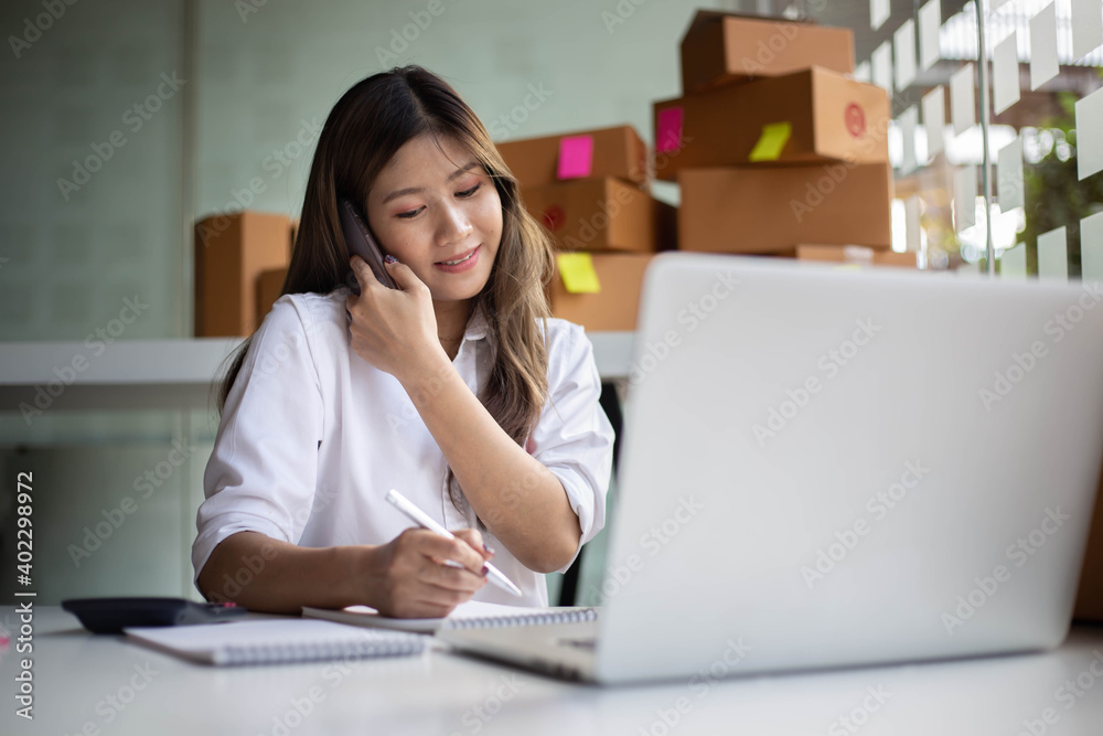 Young Asian entrepreneur owner talking on phone at workplace at home. Start up small business. Young Asian entrepreneur owner talking on phone at workplace at home. Start up small business.