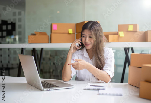 Young Asian entrepreneur owner talking on phone at workplace at home. Start up small business.