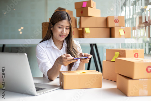 The Asian owner takes pictures of a brown package to verify his customer's address and make arrangements for delivery online while he works at home. © PaeGAG