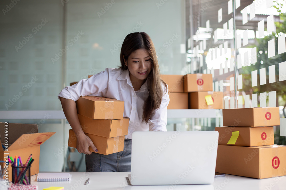 An Asian owner holds a package in a brown box, ready for delivery to a customer who orders online. As he sat in the home office An Asian owner holds a package in a brown box, ready for delivery to a customer who orders online. As he sat in the home office