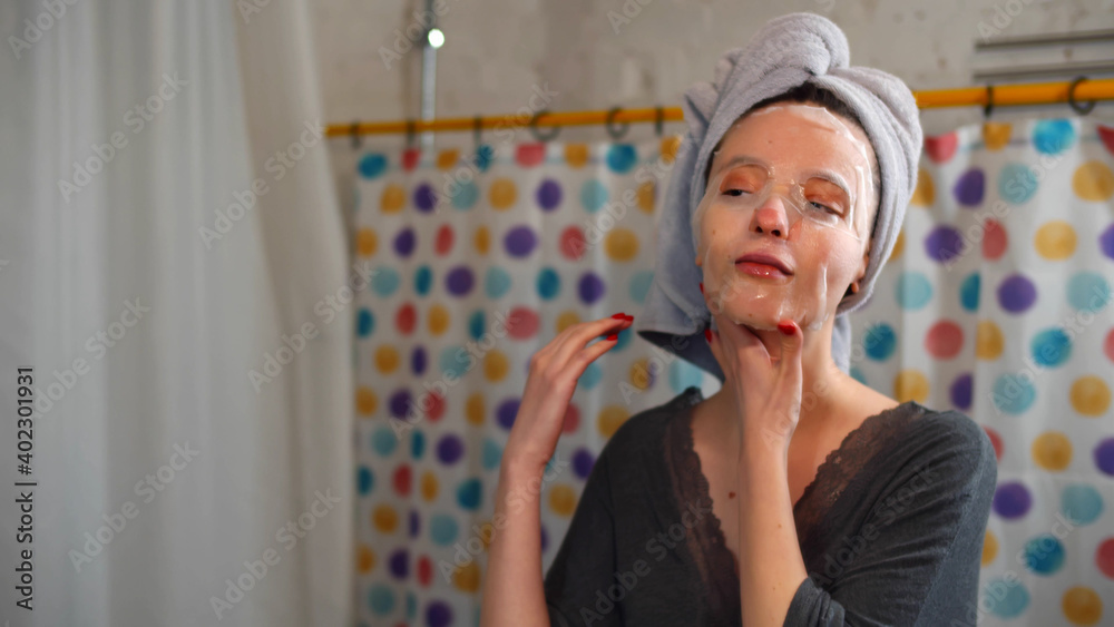 Beautiful young woman smiling and using facial mask look at mirror in bathroom Beautiful young woman smiling and using facial mask look at mirror in bathroom