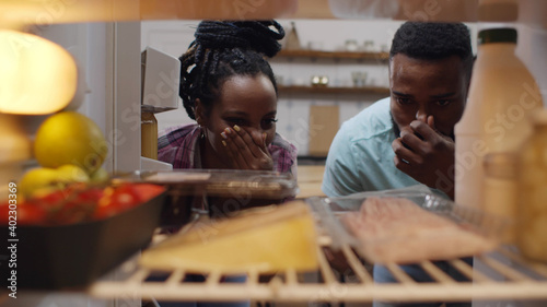 Photography Afro-american couple opening fridge and wrinkling face having food spoiled