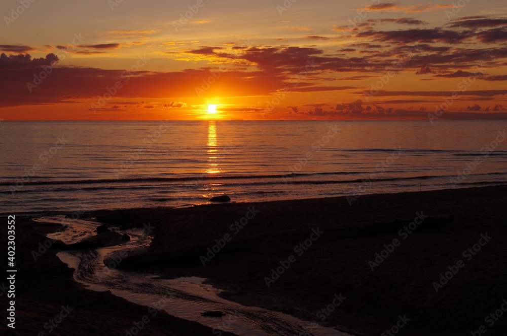 Obraz premium sea sunset with lighted clouds and small river in the foreground
