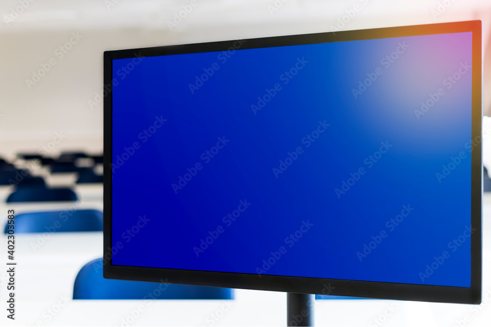 Computer monitor with blue screen, empty classroom in the background. Distance education concept.