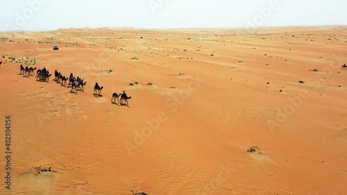 Aerial view of nomads riding camels in Sahara desert of Morocco - orbit, drone shot photo