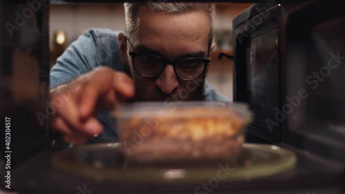 Man putting leftover dinner into microwave oven to cook photo