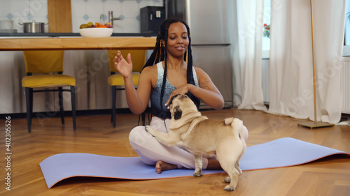 Young afro woman relaxing with sweetie dog pet doing yoga in living room at home.