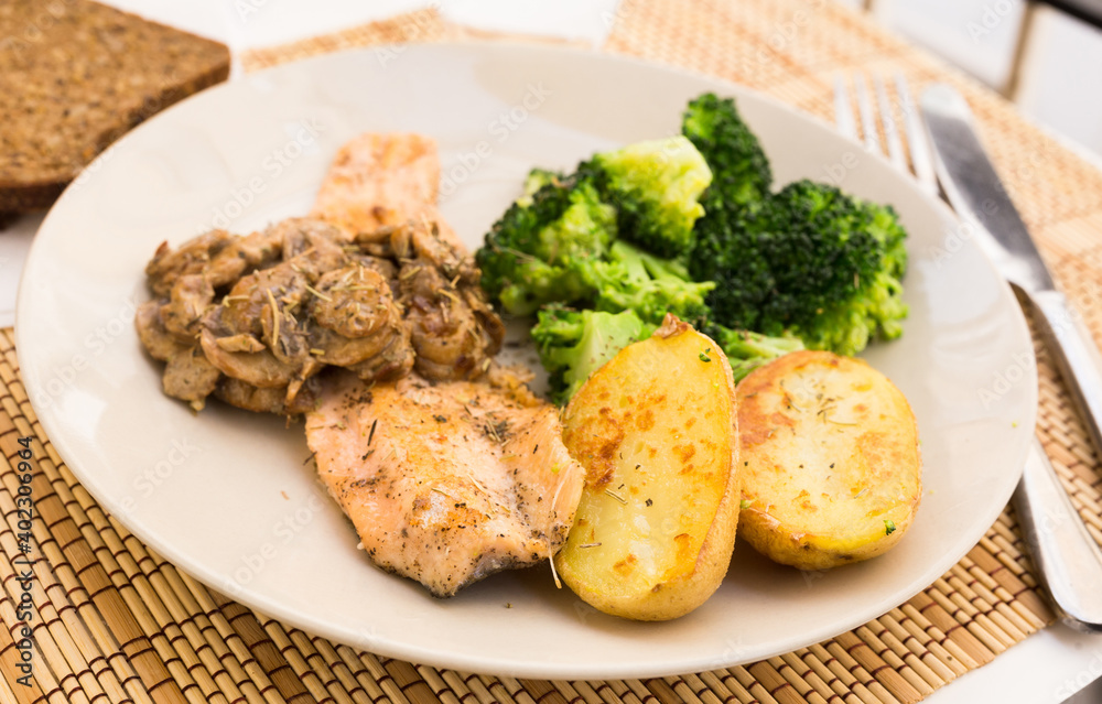 fried river trout fillet with a complex side dish of broccoli, baked potatoes and mushroom sauce