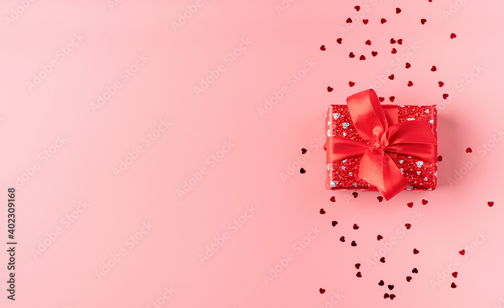 Red gift box with rope bow on pink background with heart shaped confetti top view flat lay Red gift box with rope bow on pink background with heart shaped confetti top view flat lay