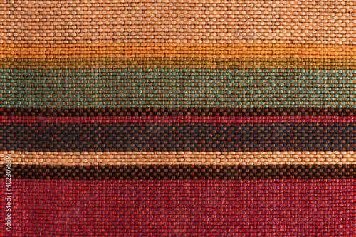 Sample of woolen fabric with red-green-yellow stripes and textured weave of threads. Blank background and close-up.