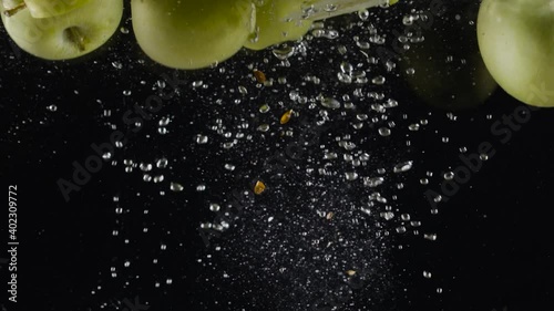 Halves of green apples in water. Action. Juicy green apples fall into water with bubbles on black background. Refreshing water with green apples photo