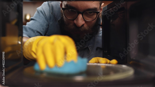 Bearded man in eyeglasses cleaning microwave oven in kitchen photo
