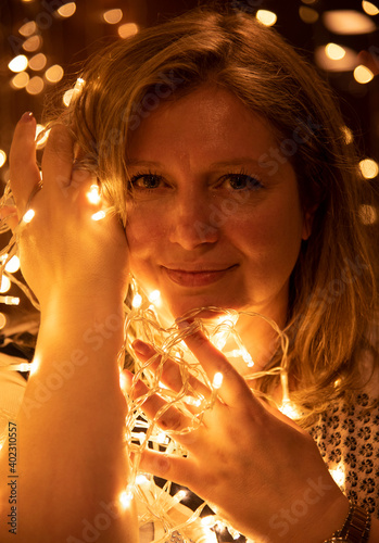 Portrait of a beautiful woman with a garland in her hands on a glowing background. © FO_DE