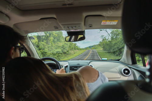 Rear view of a happy couple hugging while traveling by car - Beautiful young couple enjoying road trip together.