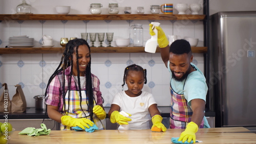 Happy african family in apron and rubber gloves cleaning kitchen surface together