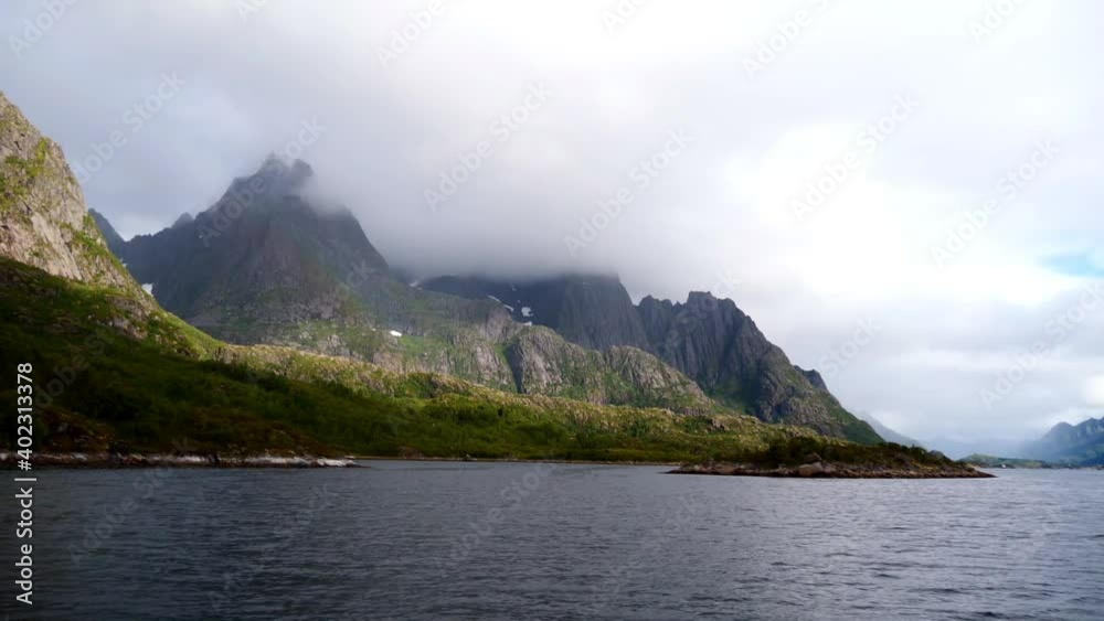 Boat cruise on Raftsundet strait in the Norwegian Sea with beautiful view of the rugged mountains of Austvågøya island, Lofoten, Norway covered by clouds in late summer. Boat cruise on Raftsundet strait in the Norwegian Sea with beautiful view of the rugged mountains of Austvågøya island, Lofoten, Norway covered by clouds in late summer.