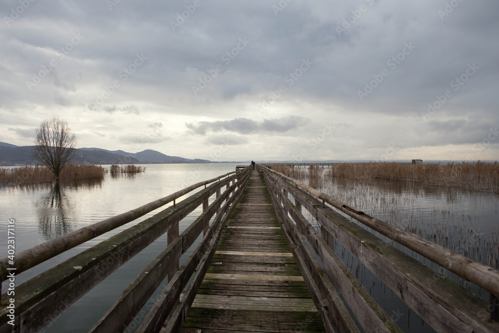 Man on wooden Pier on  Trasimeno lake in a cloudy winter day,  in the naturalistic oasis of  