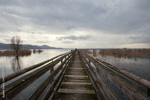 Man on wooden Pier on  Trasimeno lake in a cloudy winter day,  in the naturalistic oasis of  "La valle"   San Savino, municipality of Magione,  Umbria, Italy. © Francesca