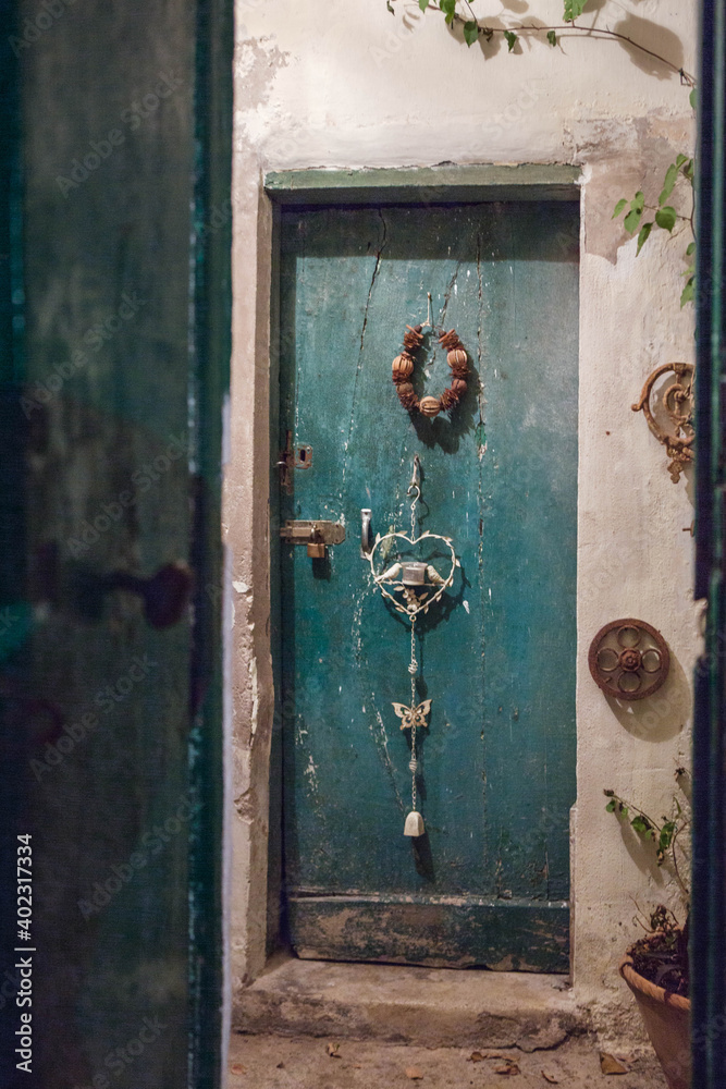 Old water-green wooden door locked illuminated at night, with a  white metal candle holder and a wreath  hanging on.