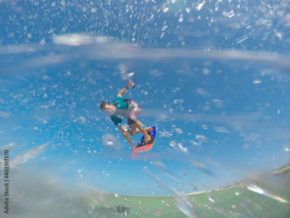 CLOSE UP: A flurry of water droplets fly towards camera as fit man kitesurfs.