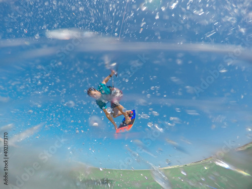 CLOSE UP: A flurry of water droplets fly towards camera as fit man kitesurfs.