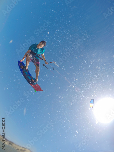 VERTICAL: Male kitesurfer splashes water at the camera while doing a trick.