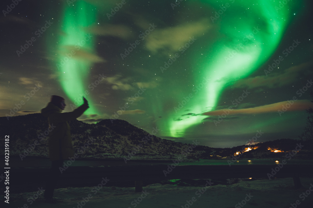 Woman with phone against glowing northern lights