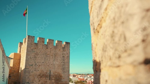 Portugal Loule stone wall reveal castle tower battlements with flag in truck camera movement under blue sky 4K photo
