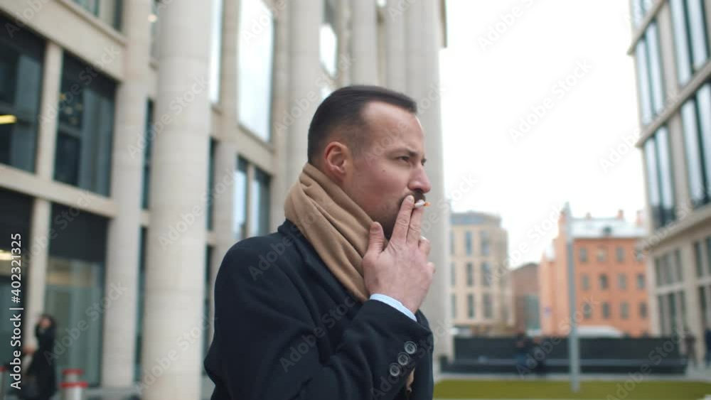 Well-dressed business man smoking standing outdoors in city Well-dressed business man smoking standing outdoors in city