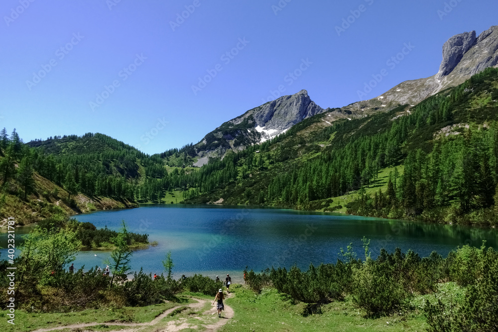 trail with hikers to a blue mountain lake in the summer