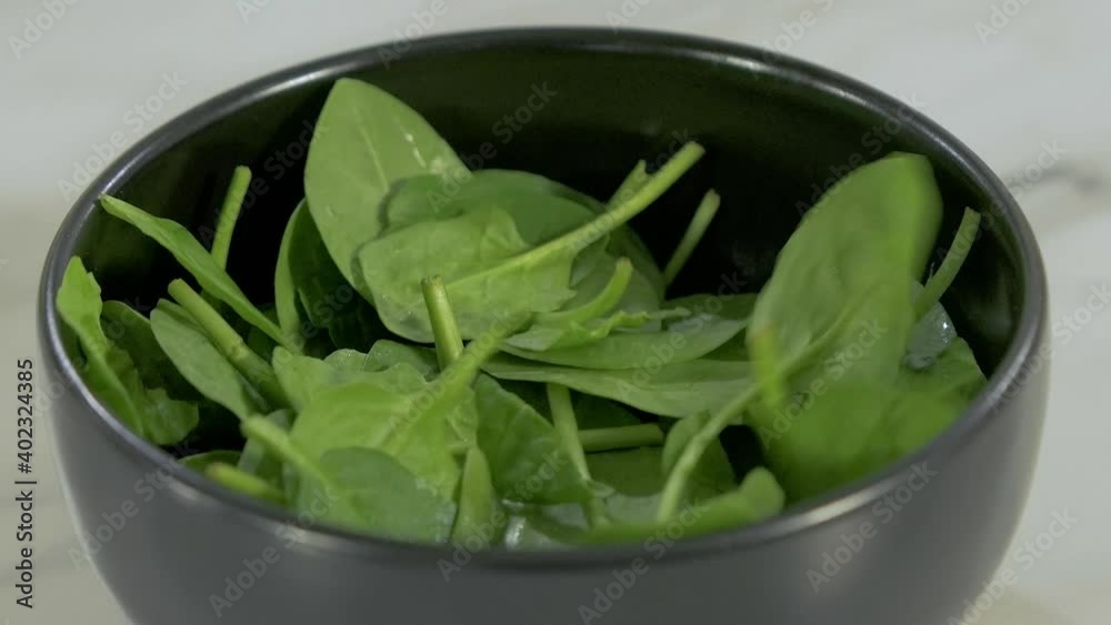 Pouring green fresh spinach to the black clay bowl, making the vegetable salad, cooking with greens, vitamin and healthy food, vegetarian meals, handheld close up shot Pouring green fresh spinach to the black clay bowl, making the vegetable salad, cooking with greens, vitamin and healthy food, vegetarian meals, handheld close up shot
