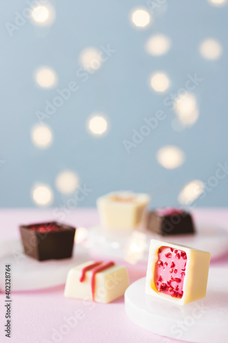 Hand decorated chocolate candy bonbons and pralines desserts on pink and blue background with lights