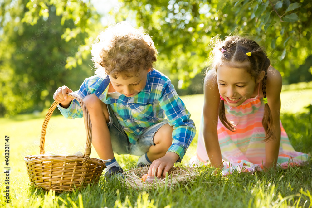 Fototapeta premium Cute boy and girl celebrating Easter, searching and eating chocolate eggs. Happy family holiday. Happy kids laughing, smiling and having fun. Beautiful spring sunny day in park