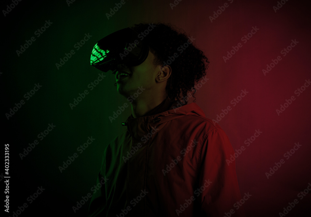 Handsome young afro man smiling with virtual reality headset in studio and colorful lighting. High-tech glasses for virtual reality.