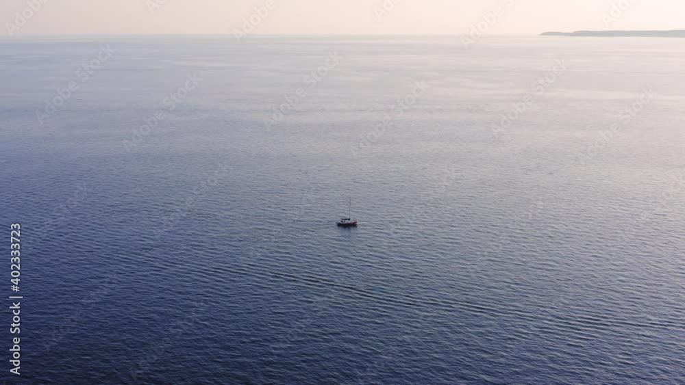Lonely boat traveling across the calm sea waters during the foggy sunset. Small island in the distance. Aerial Lonely boat traveling across the calm sea waters during the foggy sunset. Small island in the distance. Aerial