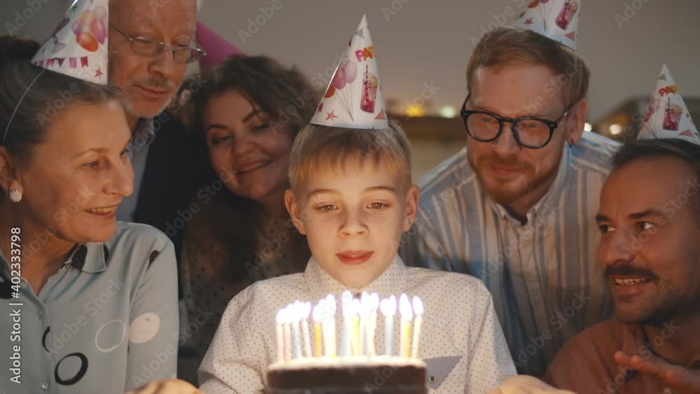 Cute boy blowing out birthday cake candles at family party